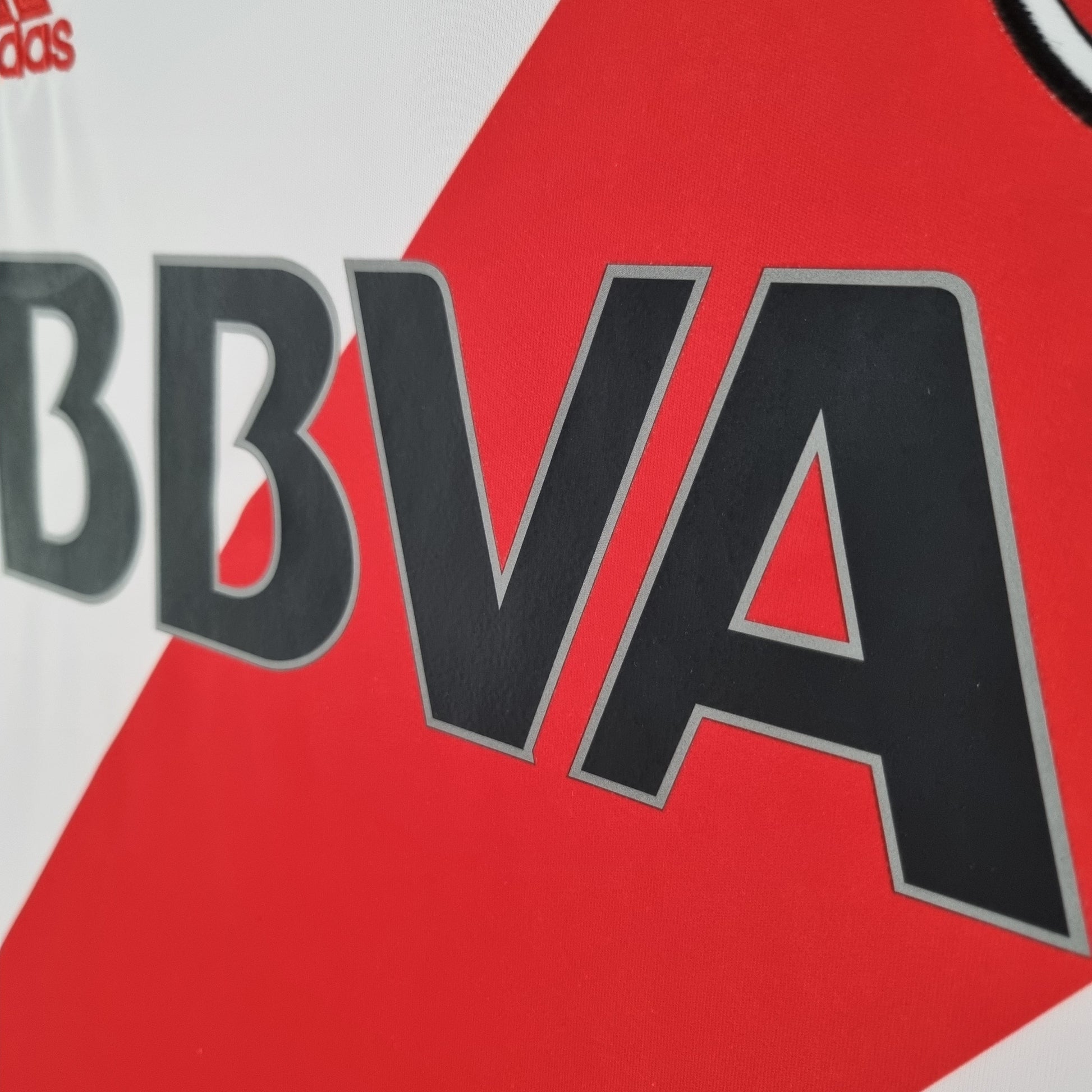 Detalle de camiseta de fútbol europea blanca y roja con logo BBVA y diseño exclusivo