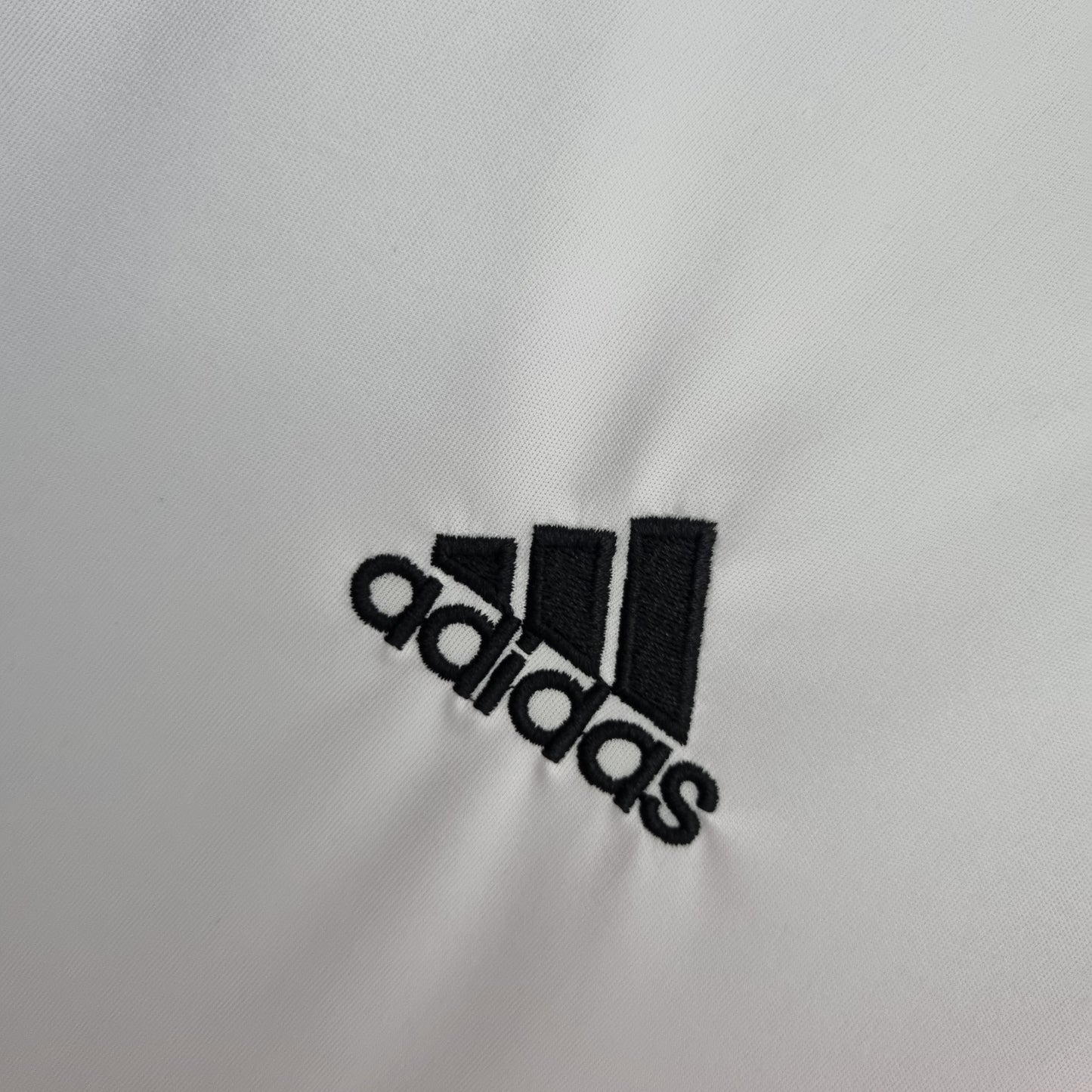 Detalle de camiseta de fútbol europea blanca con logo Adidas bordado, Reino del Futbol