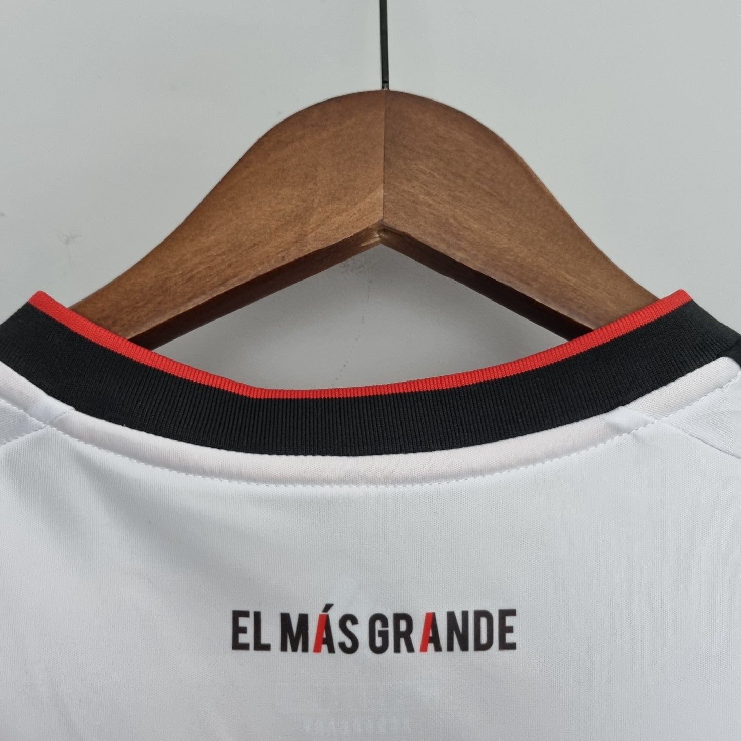 Detalle de camiseta de fútbol europea blanca con frase 'El Más Grande' en el cuello, tienda Reino del Futbol