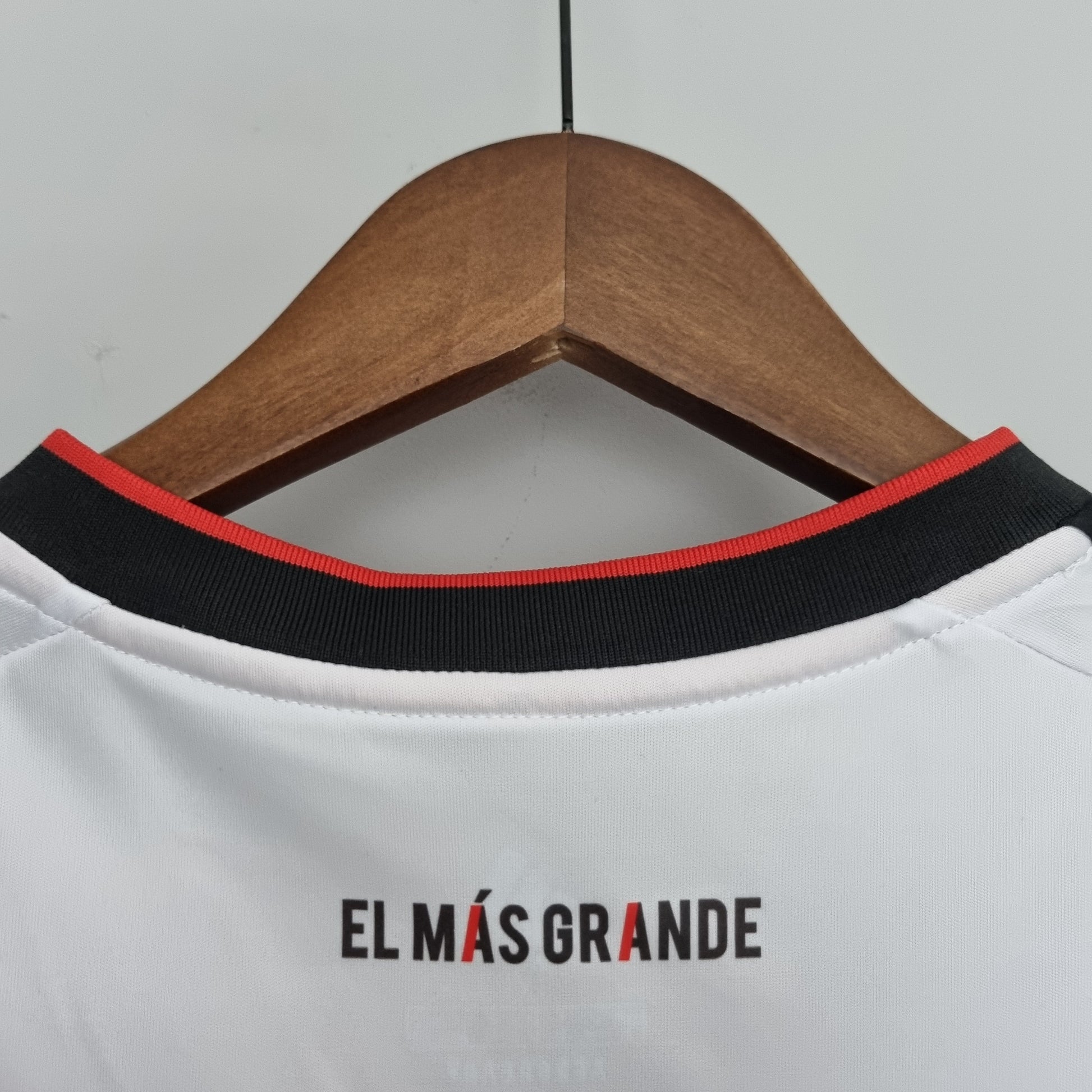 Detalle de camiseta de fútbol europea blanca con frase 'El Más Grande' en el cuello, tienda Reino del Futbol