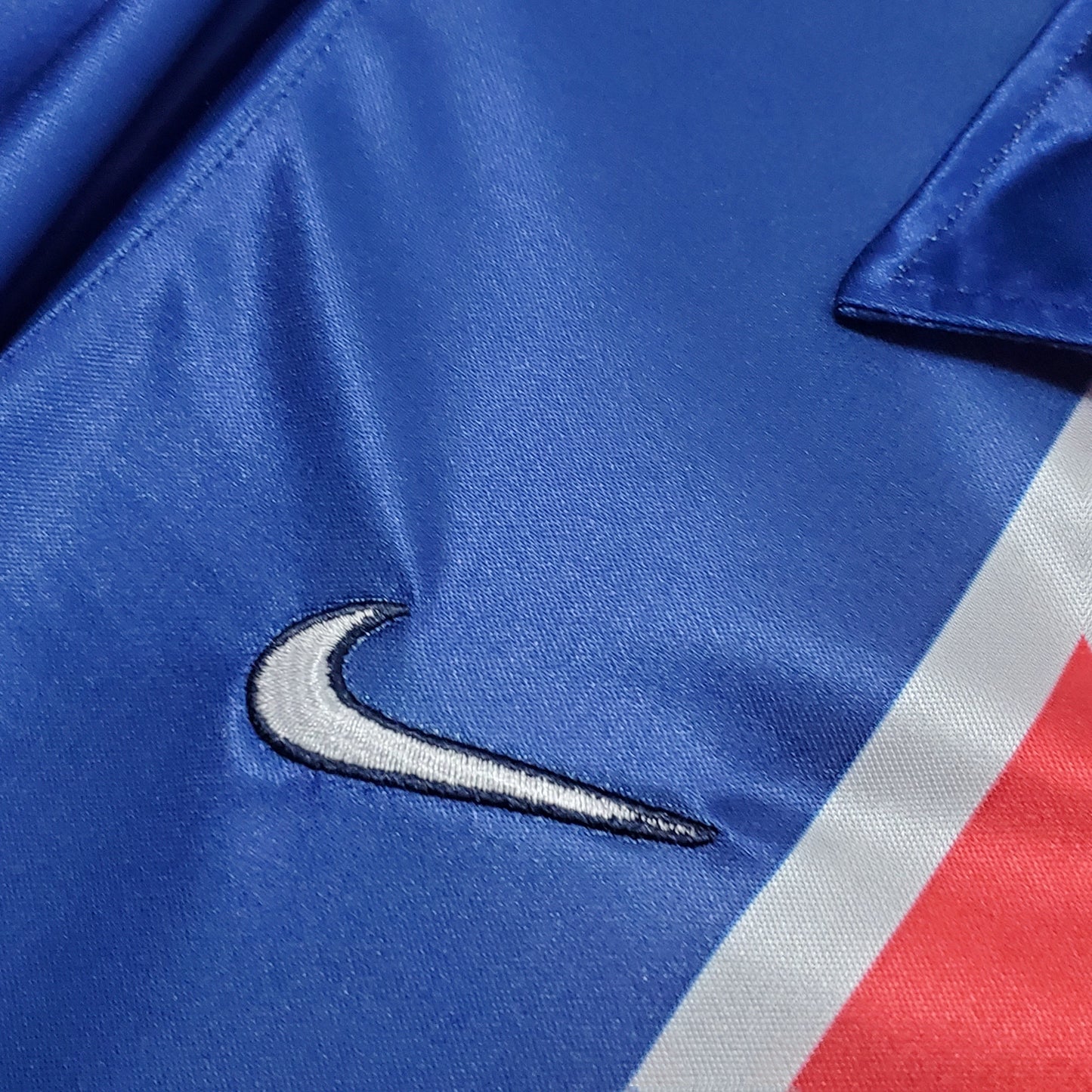 Detalle de camiseta de fútbol azul con logo Nike bordado y franja roja, Reino del Futbol
