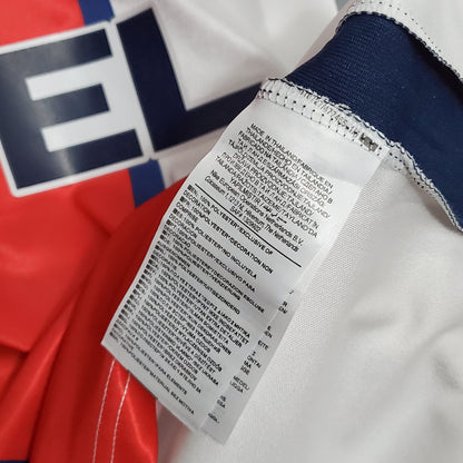 Etiqueta de camiseta de fútbol europeo, detalles de fabricación y material, fondo rojo y blanco.