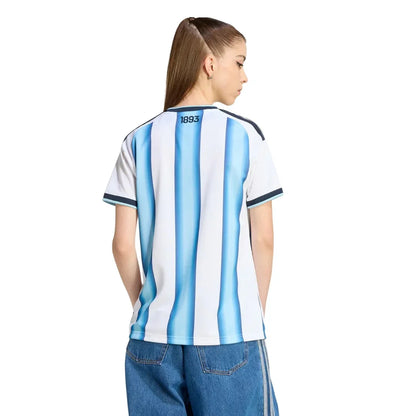 Mujer con camiseta Argentina 2026 Reino del Futbol, rayas celestes y blancas, vista trasera