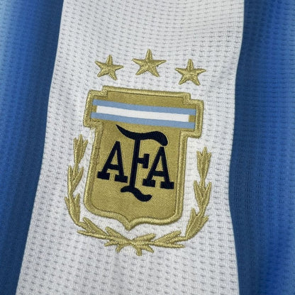 Escudo de la AFA con tres estrellas en camiseta Argentina 2026, fondo blanco y celeste