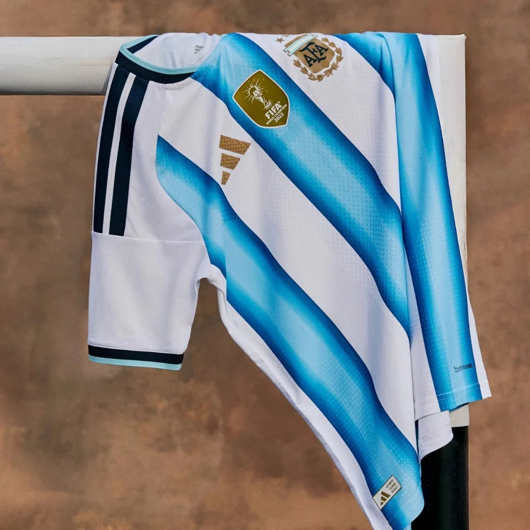 Camiseta de Argentina 2026 local blanca con franjas celestes, escudos AFA y FIFA, colgada en un poste.
