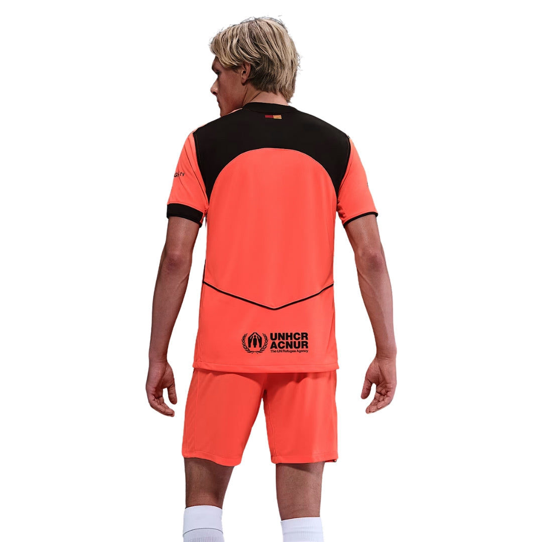 Persona con uniforme de fútbol naranja y negro, logo UNHCR ACNUR, Reino del Futbol
