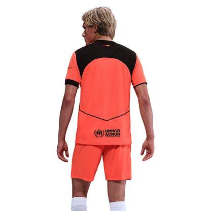 Persona con uniforme de fútbol naranja y negro, logo UNHCR ACNUR, Reino del Futbol