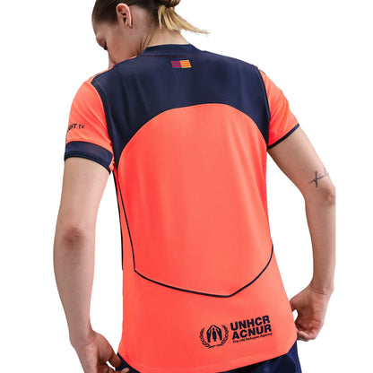 Mujer con camiseta fútbol naranja Barcelona 2025, logo UNHCR ACNUR, Reino del Futbol
