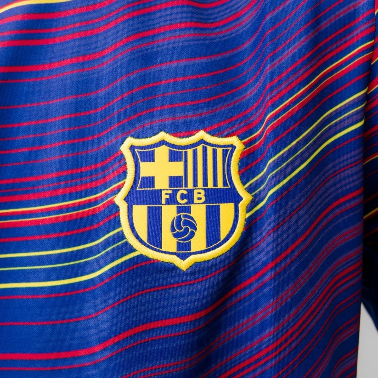 Detalle escudo FC Barcelona en camiseta entrenamiento azul con líneas rojas y amarillas, Reino del Futbol