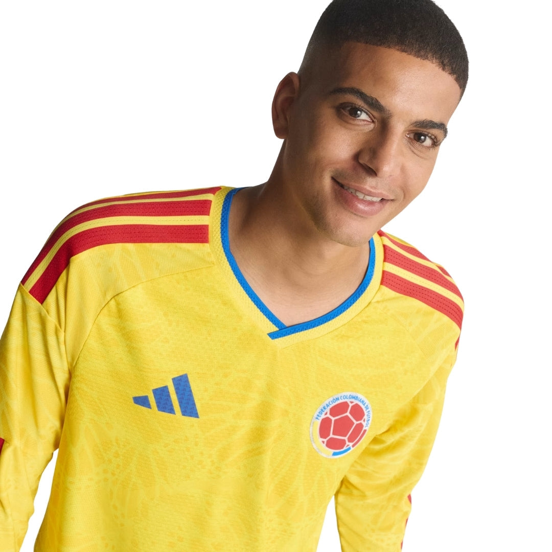 Hombre con camiseta Colombia 2026 manga larga amarilla, escudo y detalles azules y rojos.