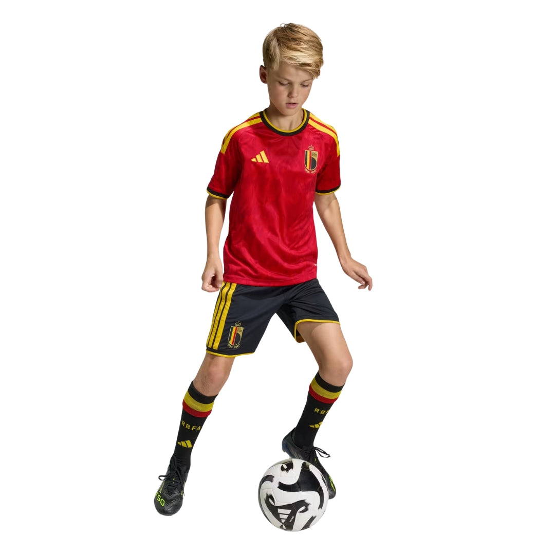 Niño con camiseta primera equipación Bélgica 2026 jugando fútbol, uniforme rojo y negro