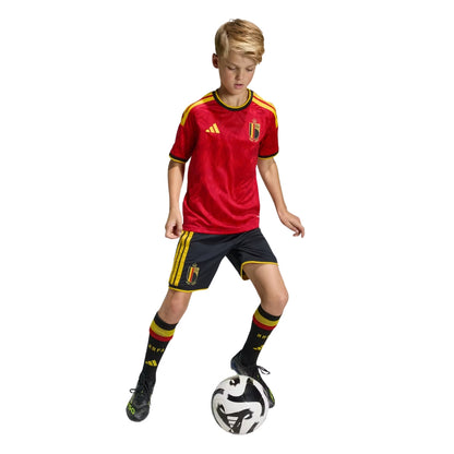 Niño con camiseta primera equipación Bélgica 2026 jugando fútbol, uniforme rojo y negro