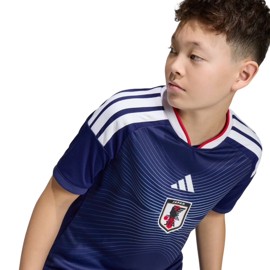 Niño con camiseta de la selección Japón 2026-2027 azul, logo JFA y rayas blancas.