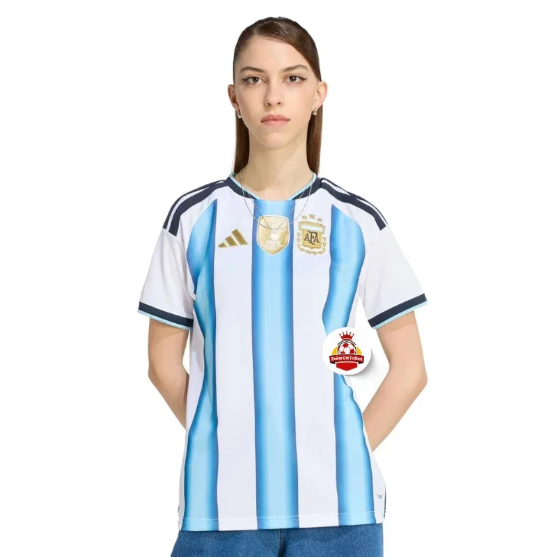 Mujer con camiseta oficial de Argentina, fondo blanco, logo Reino del Futbol visible