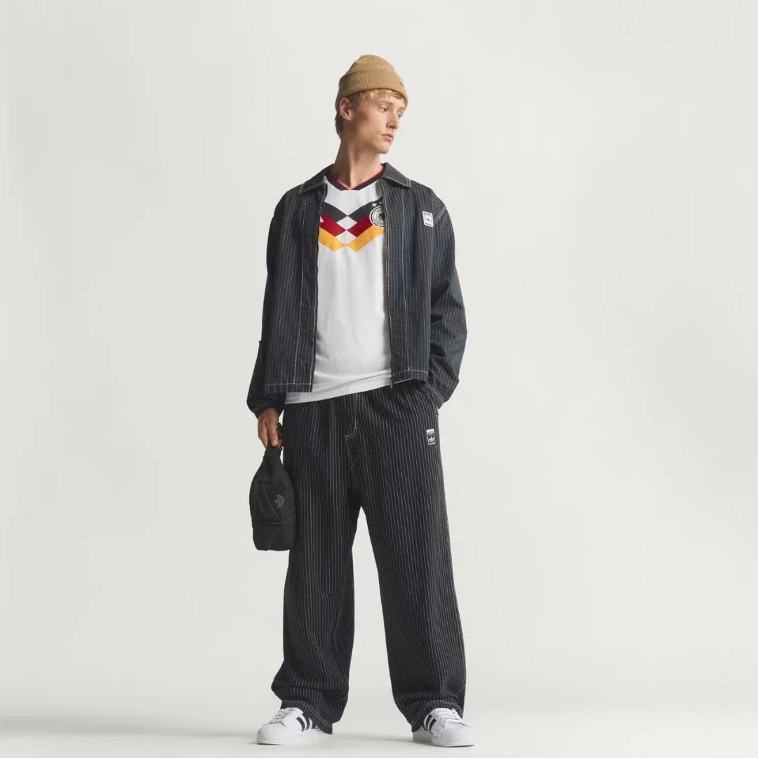 Hombre con camiseta Alemania vintage, chaqueta y pantalón a rayas, fondo blanco, Reino del Futbol