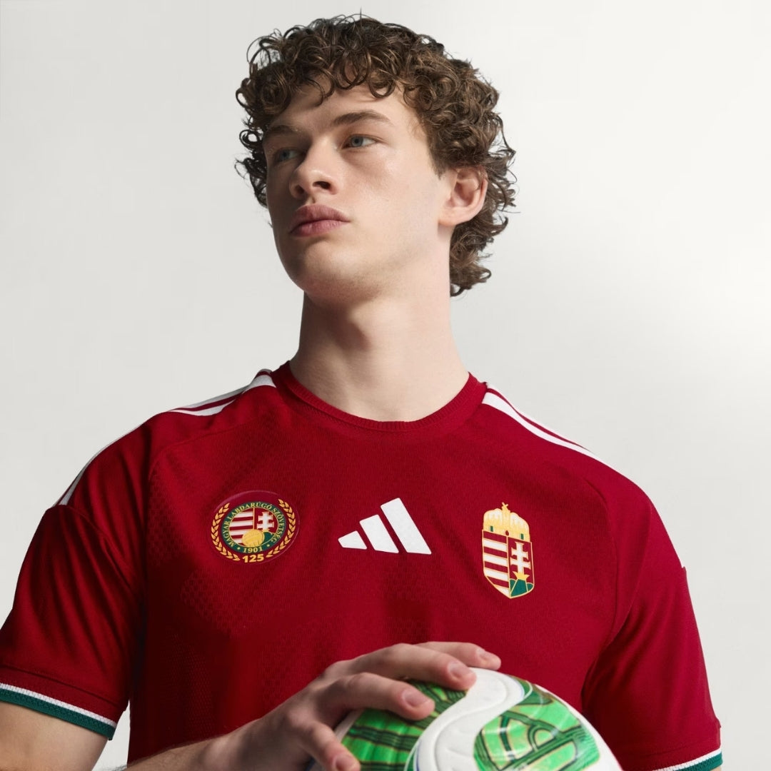 Jugador con camiseta de fútbol Hungría local 2024, logo Adidas, balón, fondo claro, Reino del Futbol