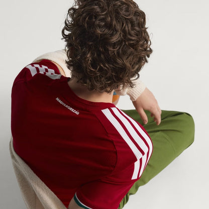 Persona con camiseta de fútbol Hungría roja, detalle de rayas blancas y texto Magyarország