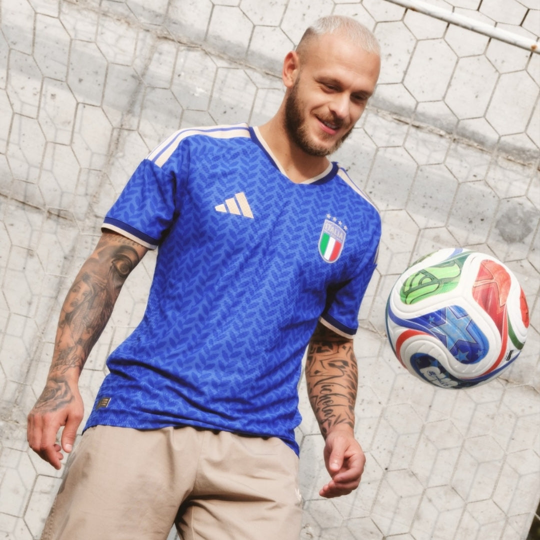 Jugador con camiseta Italia 2026 azul y balón de fútbol, fondo cancha, Reino del Futbol