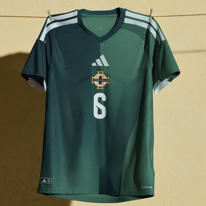 Camiseta verde Irlanda del Norte fútbol 2026 colgada, logo Adidas, número 6 en pared amarilla