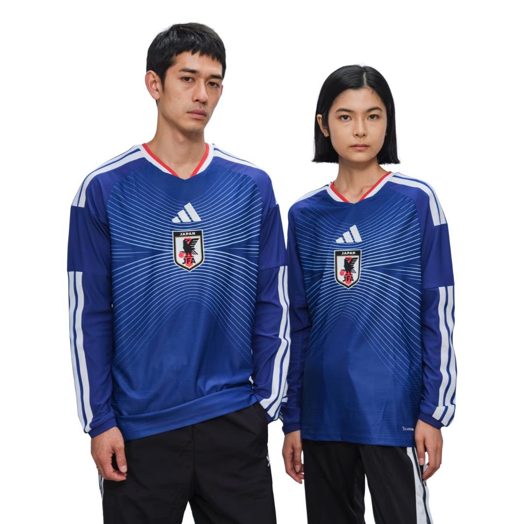 Dos personas con camiseta de fútbol Japón 2026 azul, escudo JFA visible, fondo blanco.