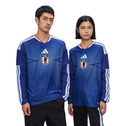 Dos personas con camiseta de fútbol Japón 2026 azul, escudo JFA visible, fondo blanco.