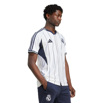Hombre vistiendo camiseta de fútbol Real Madrid blanca con rayas, ropa deportiva europea.