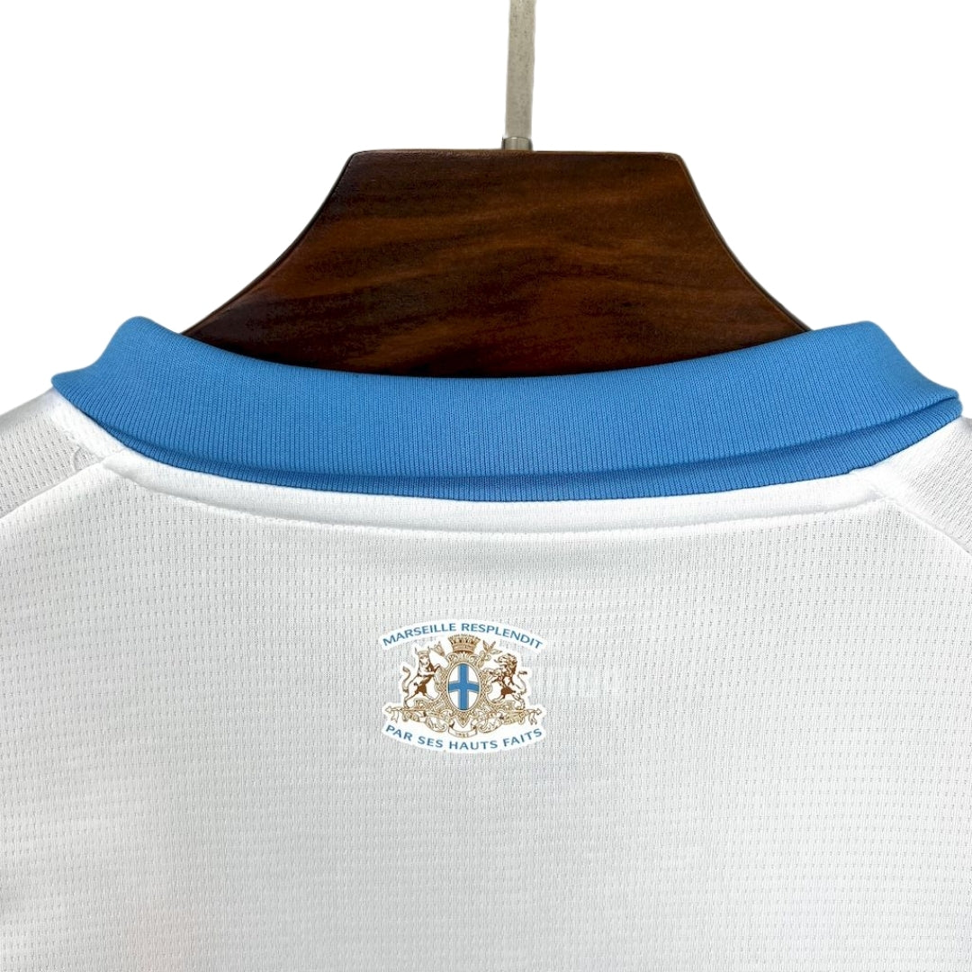 Detalle de la parte trasera de la camiseta Olympique Marsella 2025-26 blanca con cuello azul, escudo y lema.