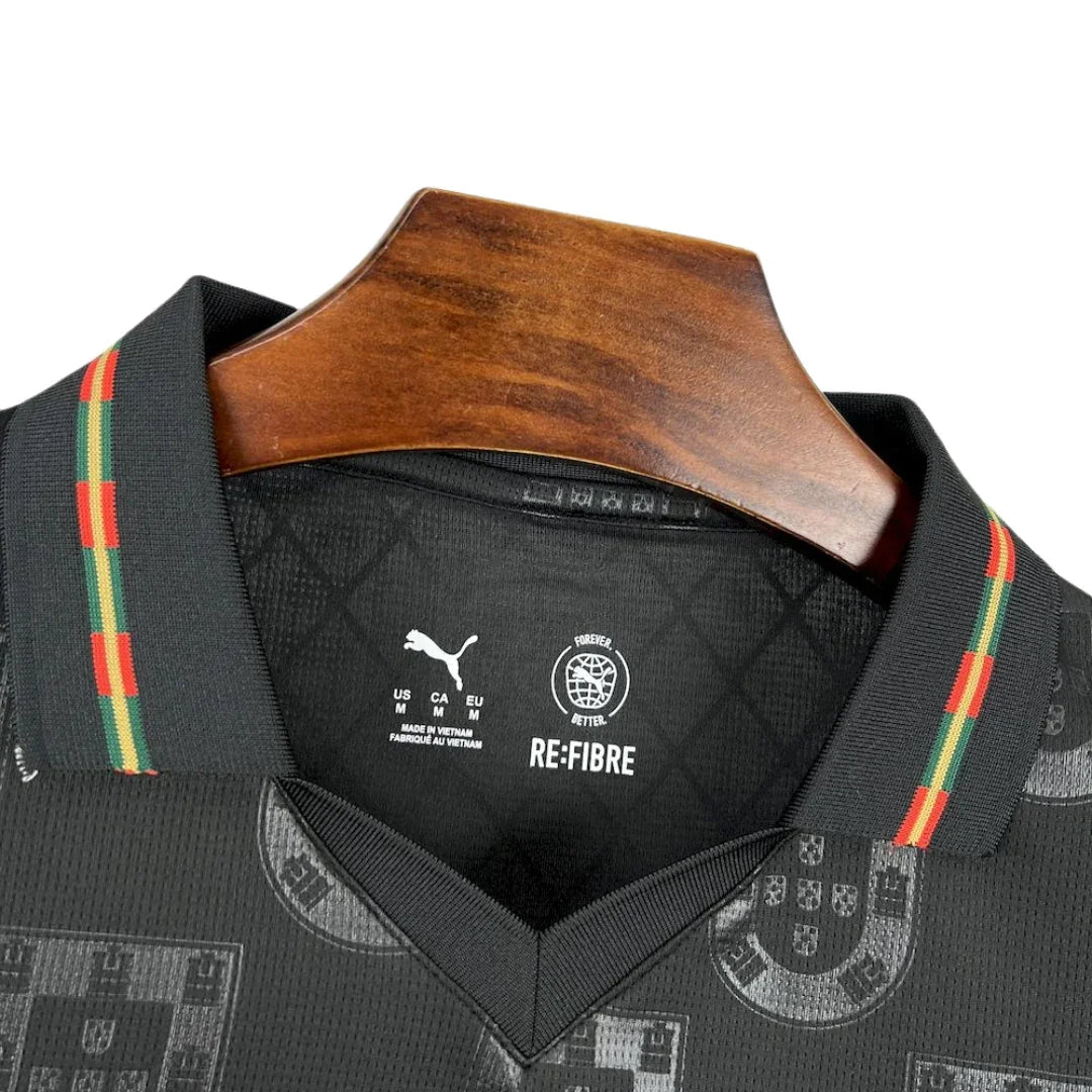 Camiseta de fútbol negra Portugal Puma Re-Fibre con detalles verdes y rojos, en percha de madera
