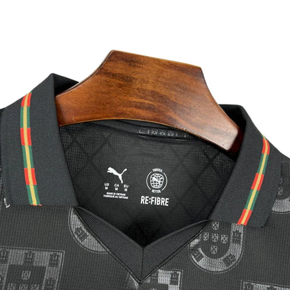 Camiseta de fútbol negra Portugal Puma Re-Fibre con detalles verdes y rojos, en percha de madera