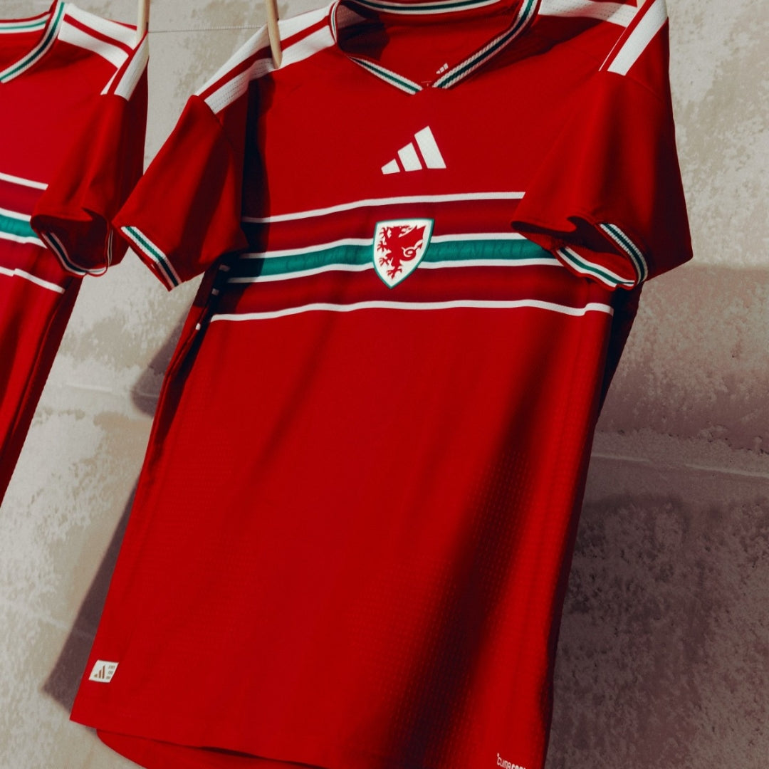 Camiseta roja de fútbol de País de Gales con logo de dragón, diseño Adidas, colgada en pared