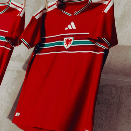 Camiseta roja de fútbol de País de Gales con logo de dragón, diseño Adidas, colgada en pared