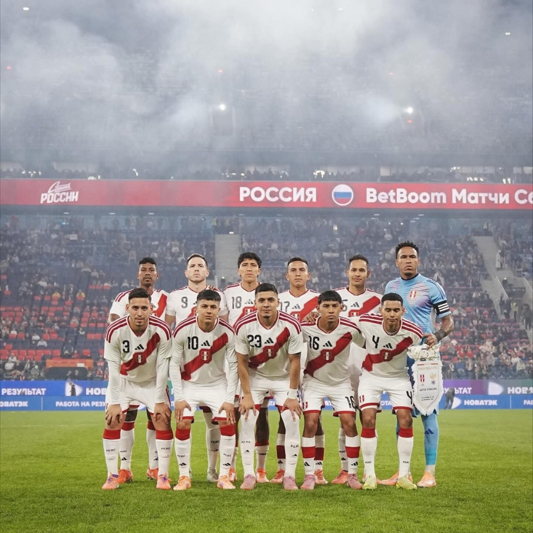 Selección nacional de fútbol de Perú con uniforme blanco y franja roja en estadio lleno, Reino del Futbol.