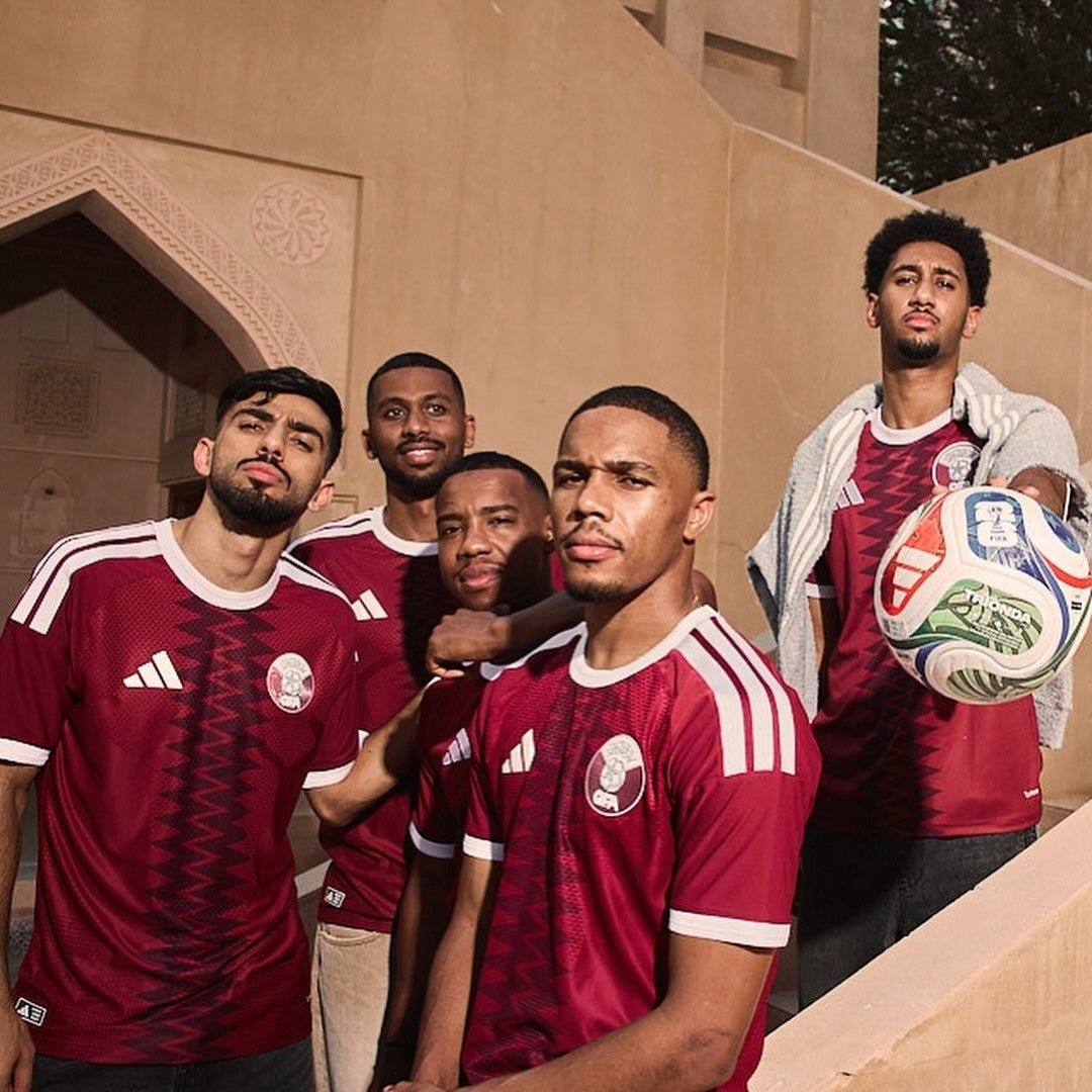 Jugadores con camiseta de fútbol Qatar 2026, balón y arquitectura árabe, Reino del Futbol