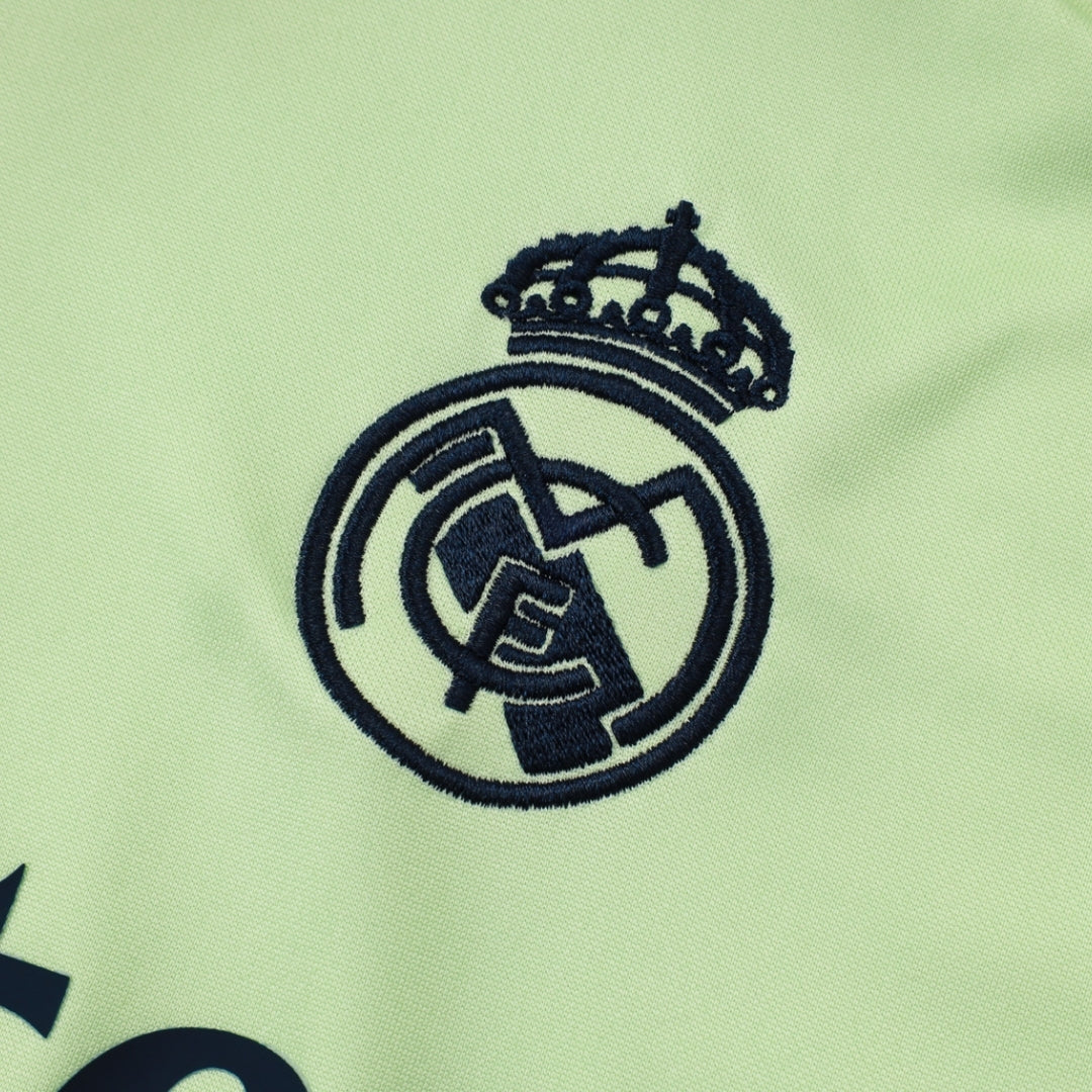 Escudo bordado del Real Madrid sobre tela verde claro, detalle de sudadera deportiva.