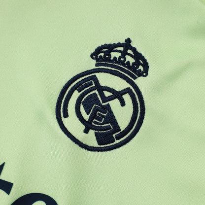 Escudo bordado del Real Madrid sobre tela verde claro, detalle de sudadera deportiva.
