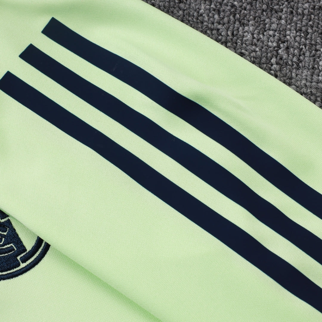 Detalle de manga verde claro con franjas negras y escudo de equipo en sudadera deportiva