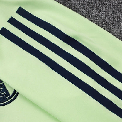 Detalle de manga verde claro con franjas negras y escudo de equipo en sudadera deportiva