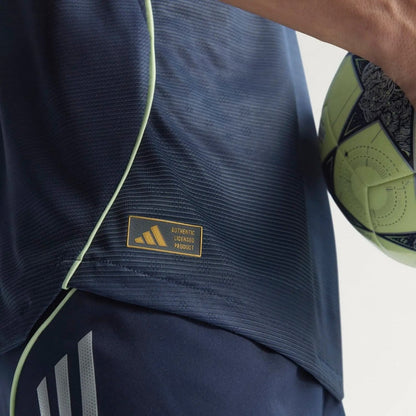 Detalle de camiseta Real Madrid 25/26 versión jugador azul marino Adidas con balón de fútbol