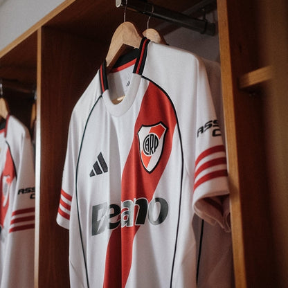 Camiseta River Plate 2026 blanca con banda roja colgada en vestuario, venta Reino del Futbol