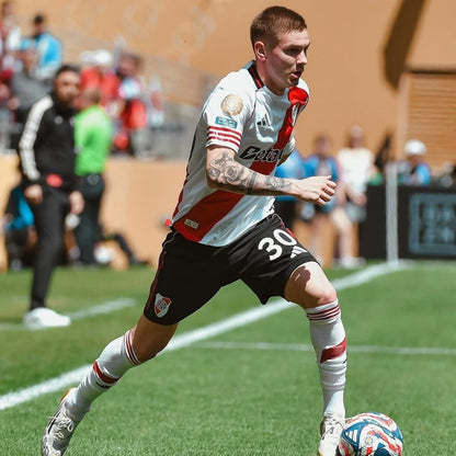 Jugador de River Plate 2026 con camiseta blanca y roja, jugando fútbol en campo, Reino del Fútbol.