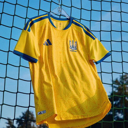 Camiseta Ucrania 2026 de fútbol amarilla colgada en red, Reino del Futbol