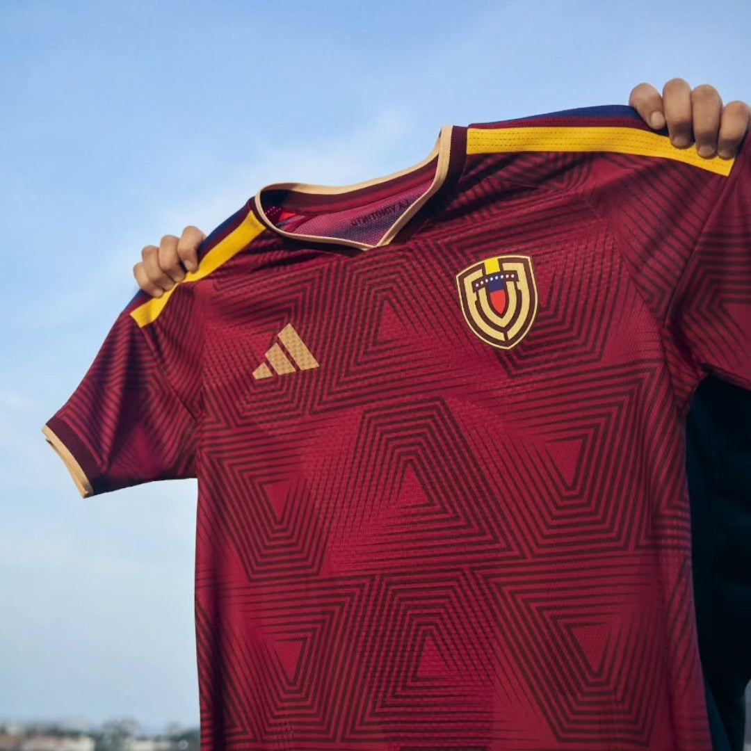 Camiseta oficial Vinotinto Venezuela 2026, escudo y diseño geométrico, cielo azul de fondo