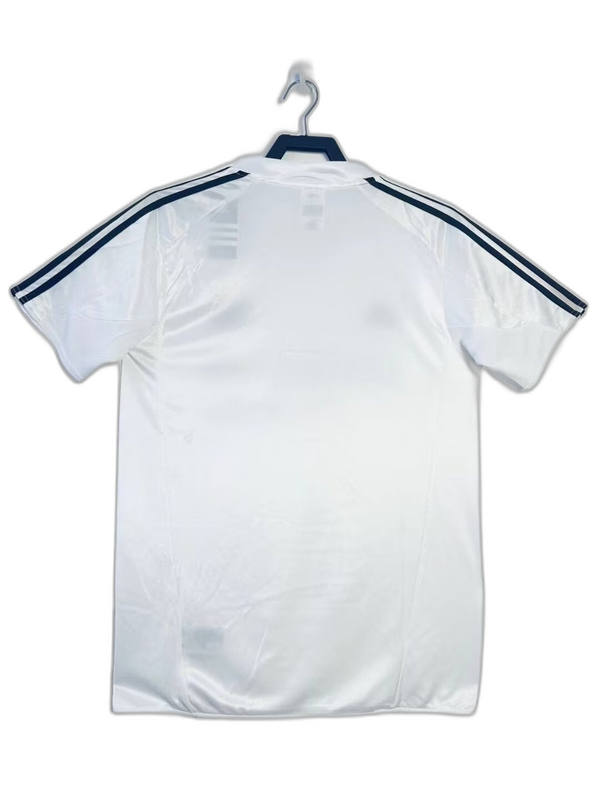 Camiseta retro Real Madrid 2004-2005 blanca con rayas negras en las mangas, exhibida en gancho