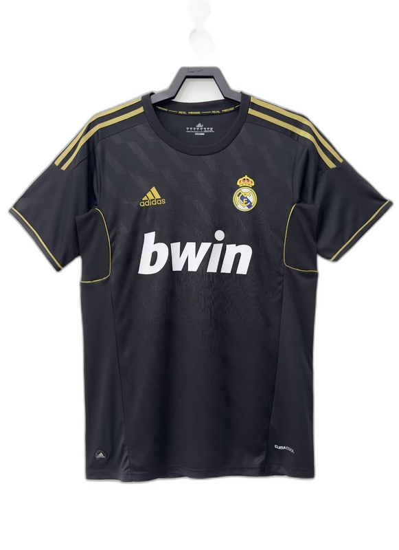 Camiseta Real Madrid visitante 2011-2012 negra, detalles dorados, logo Adidas y escudo del club.