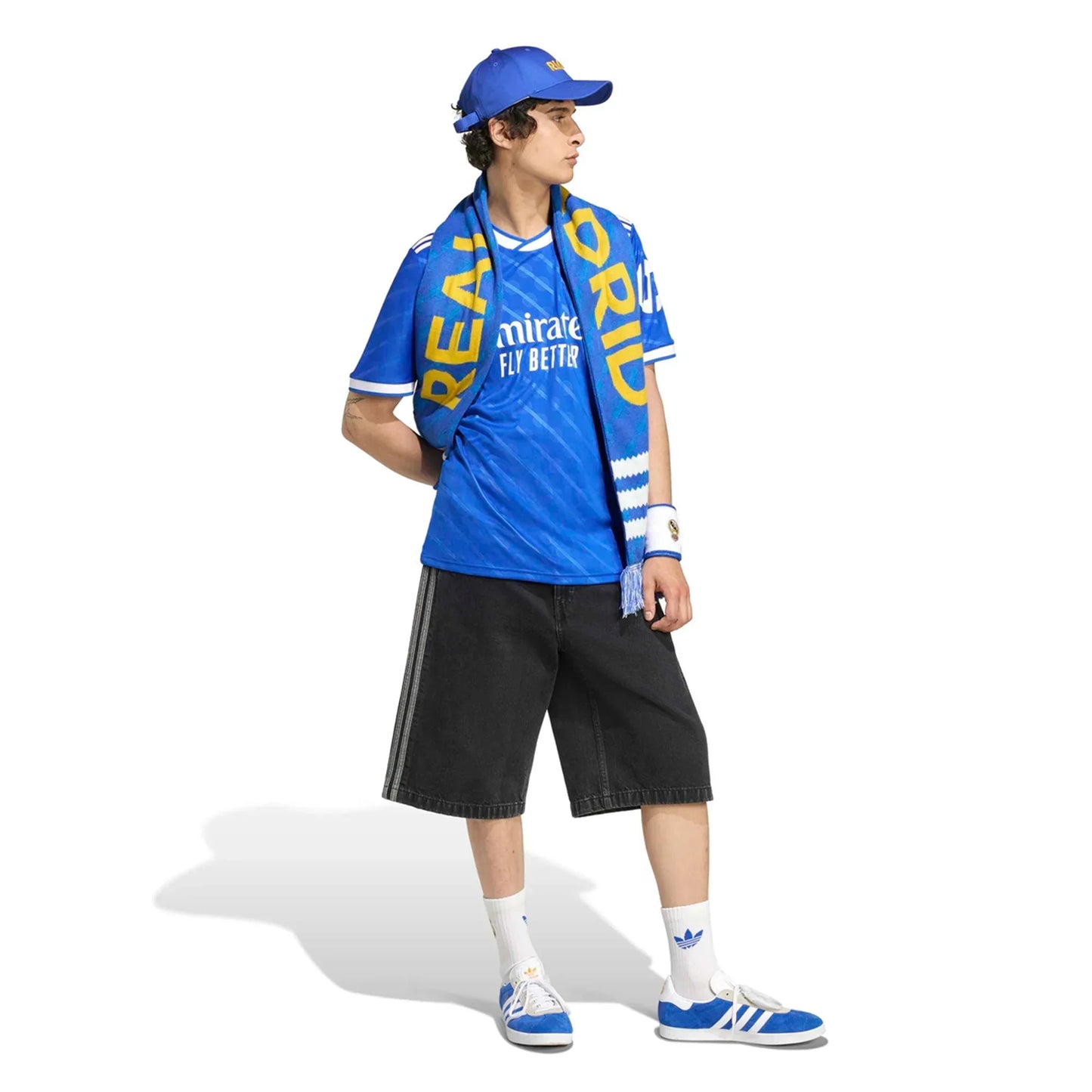 Aficionado con camiseta azul del Real Madrid, bufanda, gorra y zapatillas Adidas, moda fútbol.
