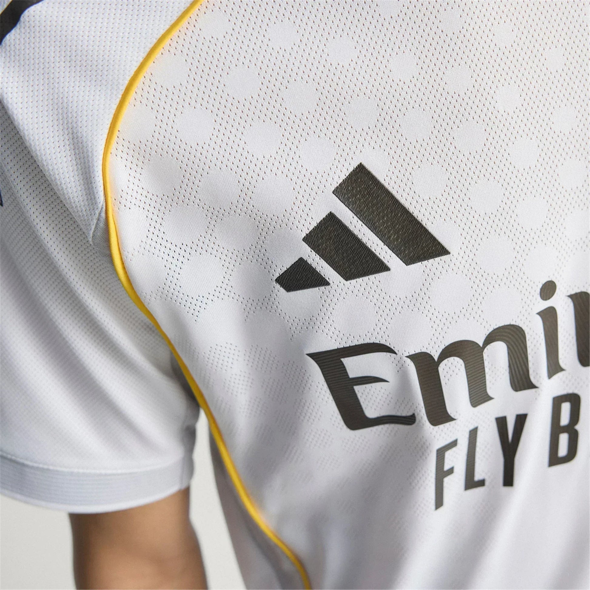 Detalle de camiseta de fútbol europea blanca con logo Adidas y ribete amarillo, Reino del Futbol